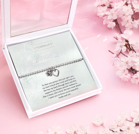 Silver beaded bracelet with heart and flower charms, displayed in a white gift box alongside a card titled 