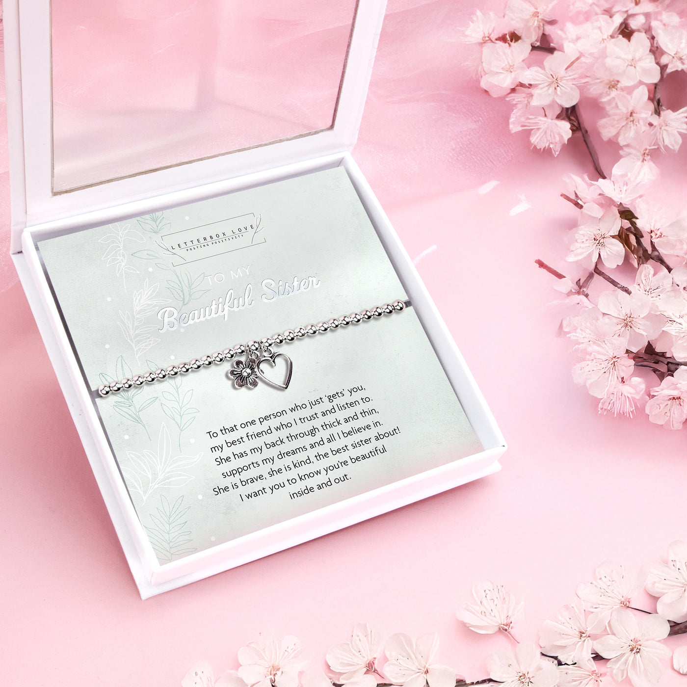 Silver beaded bracelet with heart and flower charms, displayed in a white gift box alongside a card titled 