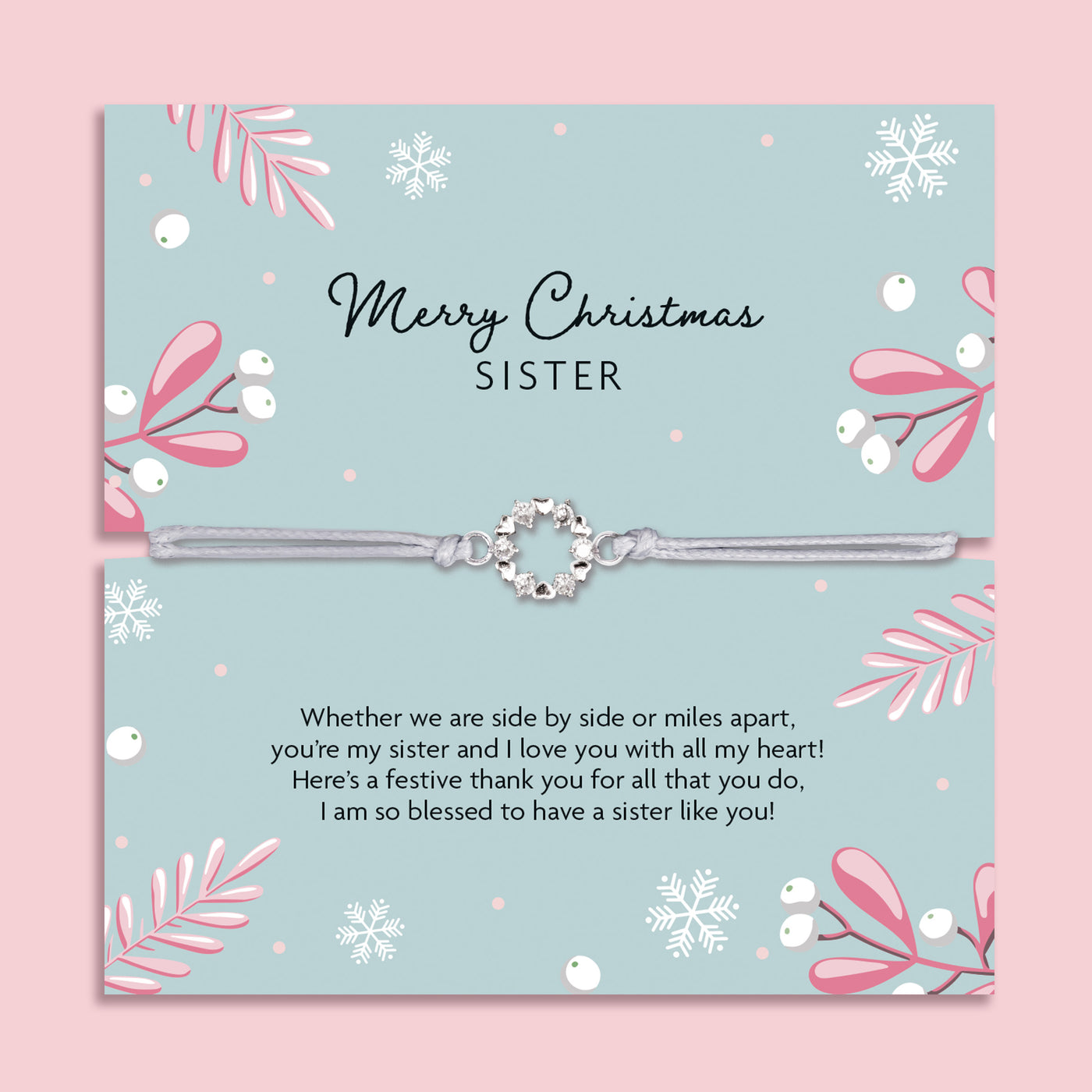 Merry Christmas Sister bracelet featuring a silver wreath charm on an adjustable cord, presented on a festive green card with snowflakes, mistletoe, and pink leaves. Includes a soft white pouch for gifting and safekeeping. A sentimental Christmas jewellery gift for sisters, perfect as a stocking filler.