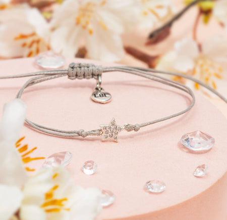 Bracelet with star charm on a pink surface with flowers and water droplets