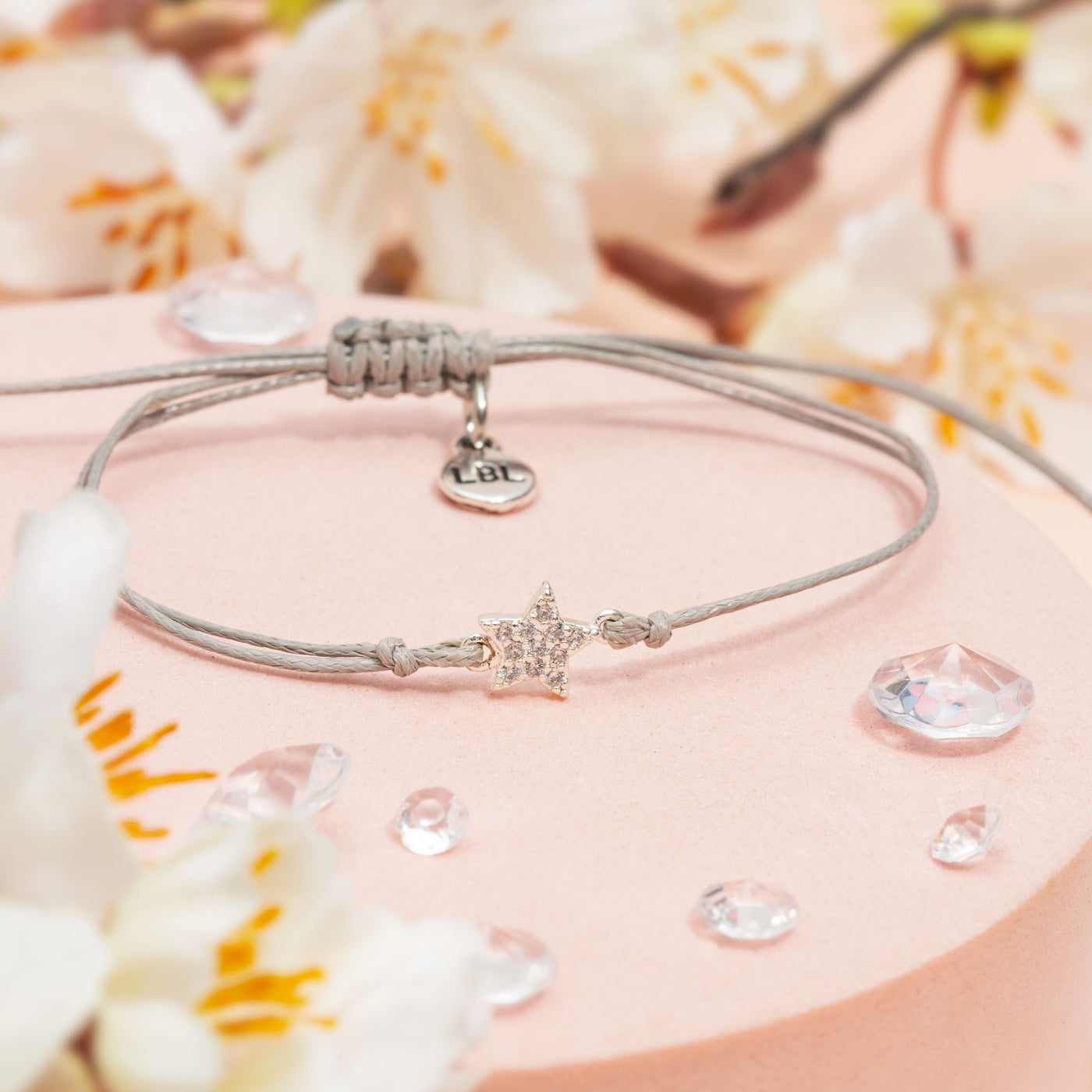 Bracelet with star charm on a pink surface with flowers and water droplets