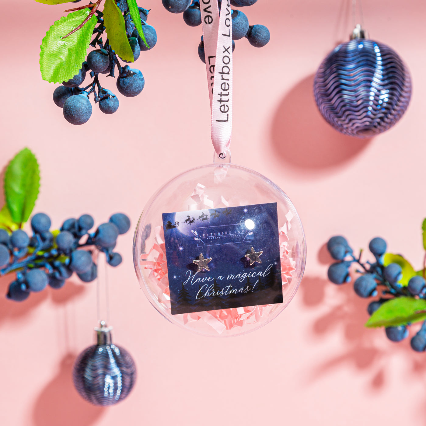 Transparent Christmas bauble tied with a 'Letterbox Love' ribbon, displaying a card with a message 'Have a magical Christmas!' and a pair of star-shaped earrings,