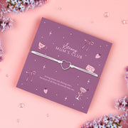 A purple adjustable bracelet featuring a  heart charm, displayed on a purple backing card with the message "Strong Mum's Club" and the poem: "Strong Mums are shining stars, because of all they do and all they are." Surrounded by lilac flowers. Perfect for gifting to mums.