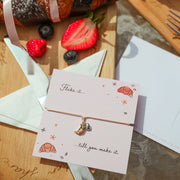 Baked goods with a pink bow on a wooden board, accompanied by a card with a message.