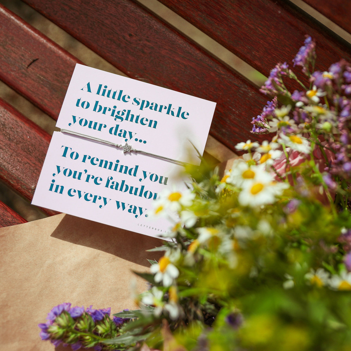 Card with a message and a small gift on a wooden surface with flowers.