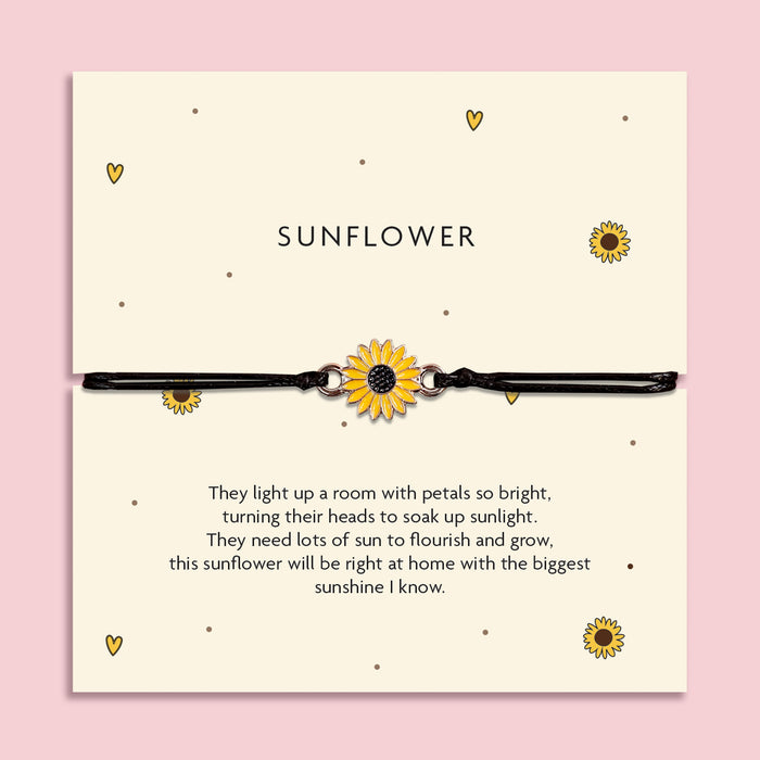 Adjustable black cord bracelet with a yellow sunflower charm, displayed on a cream card titled 'Sunflower'. The card features a cheerful poem about brightness, growth, and sunshine. Surrounded by flowers on a pink background, this is a joyful gift from Letterbox Love.