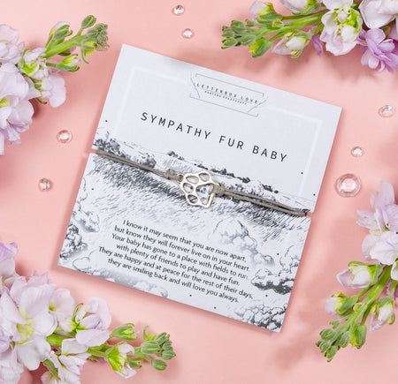A heartfelt sympathy card titled 'Sympathy Fur Baby' surrounded by soft grey clouds and field.  The card features a touching message of remembrance and a delicate silver paw print charm.