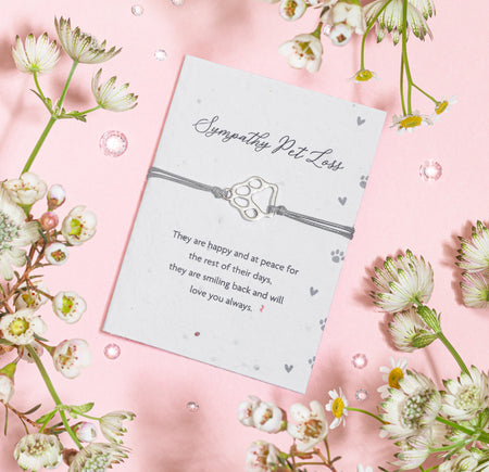 A sympathy seed paper card for pet loss, featuring a paw print charm on a gray bracelet with the inscription 