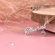 Detail of a silver 'Taurus' bracelet with a heart charm on a pink background. Zodiac bracelet for a friend. 