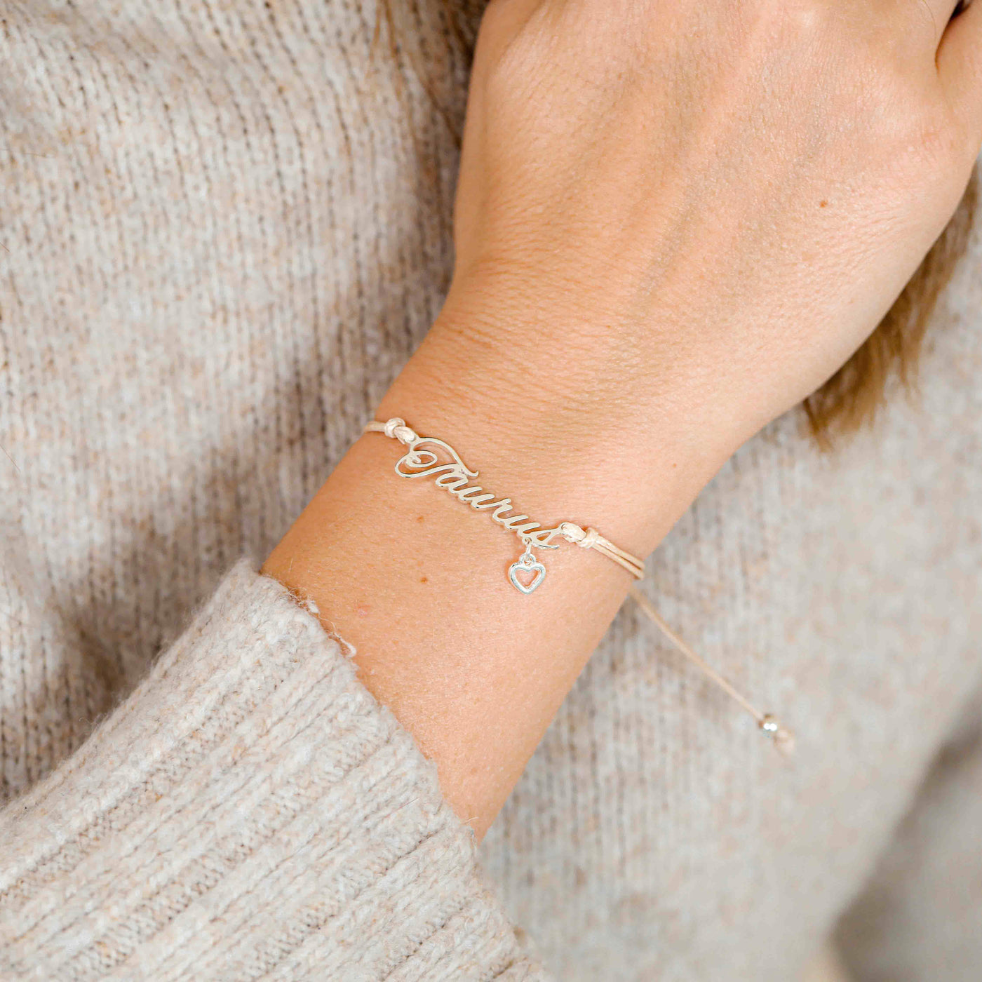 A woman wearing a delicate bracelet with the word “Taurus” and a small heart charm, a thoughtful zodiac bracelet gift for her.