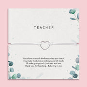 A teacher-themed gift card with a silver heart-shaped cord bracelet across the center. The card has a textured off-white background, watercolor eucalyptus leaves in the corners, and a printed message at the bottom.