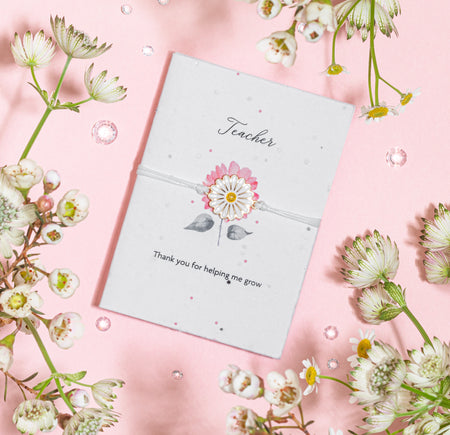 A white daisy charm bracelet elegantly placed on a seed paper greeting card with 
