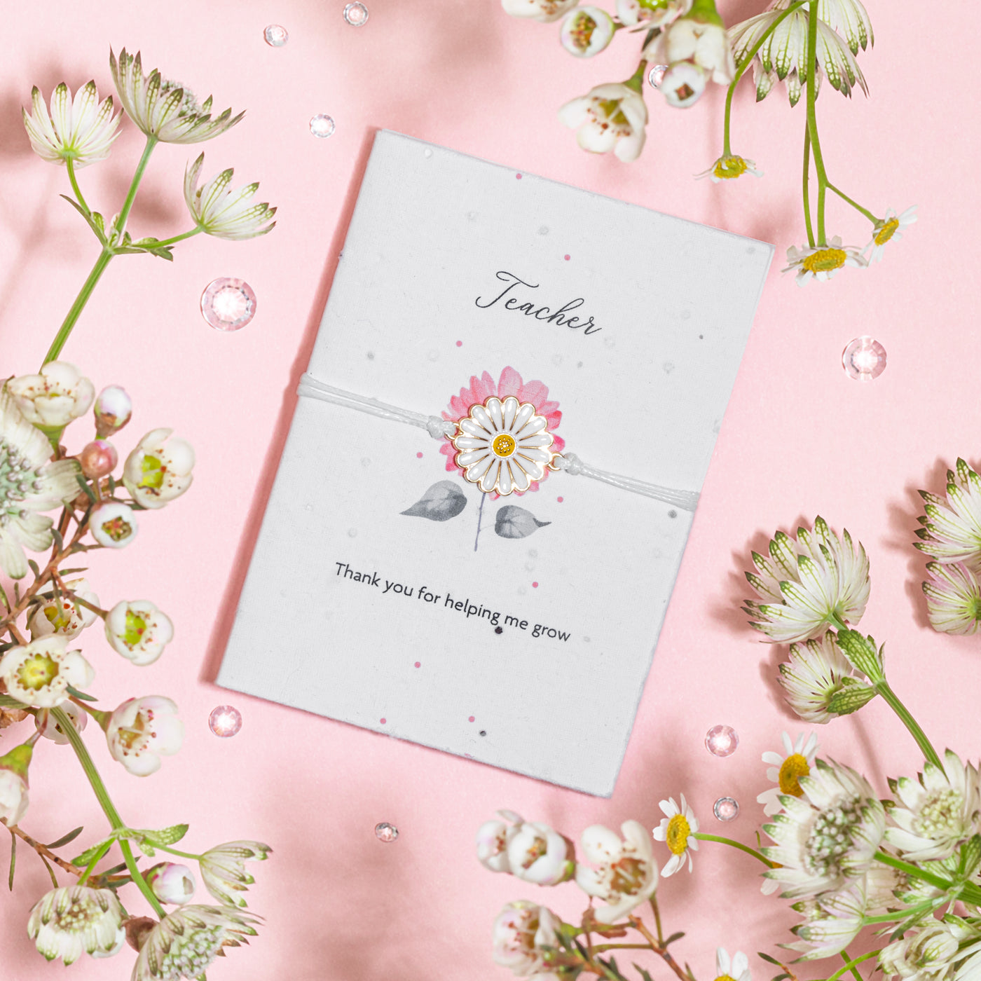 A white daisy charm bracelet elegantly placed on a seed paper greeting card with 