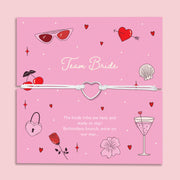 Team Bride hen party bracelet – cute silver heart charm on white cord, displayed on a fun pink card with cocktail, cherry, and love heart designs. Perfect for bridesmaid proposal boxes, hen do favours, bride tribe accessories, or bottomless brunch party gifts. Affordable letterbox jewellery for bachelorette celebrations.