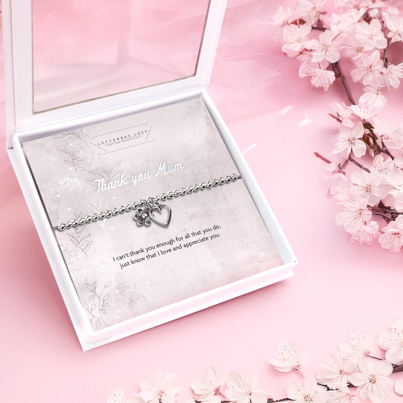 Silver beaded bracelet with heart and flower charms, presented in a white gift box alongside a card titled 