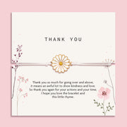 Elegant 'Thank You' card on a blush pink backdrop, adorned with a daisy-inspired bracelet. The card showcases delicate floral illustrations and a heartfelt gratitude message. 