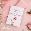 Pink cord bracelet with a silver heart charm, presented on a 'Thank you for being you' card featuring an illustration of a bunny holding heart-shaped balloons. A sweet and thoughtful gift for expressing gratitude and love.