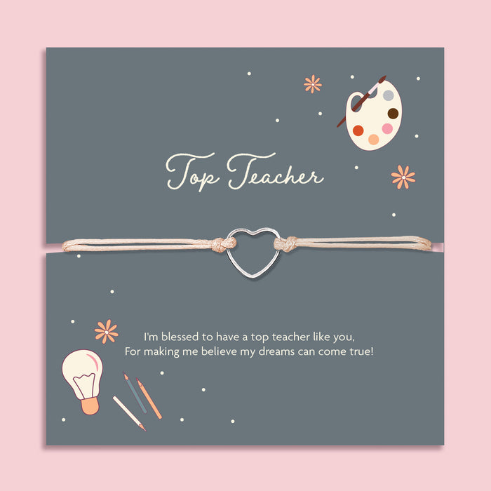 Cream adjustable cord bracelet with a silver open heart charm, displayed on a navy blue card with the message 'Top Teacher'. The card features illustrations of a paint palette, lightbulb, and pencils, with a thank you note for inspiring dreams. A thoughtful teacher appreciation gift from Letterbox Love.