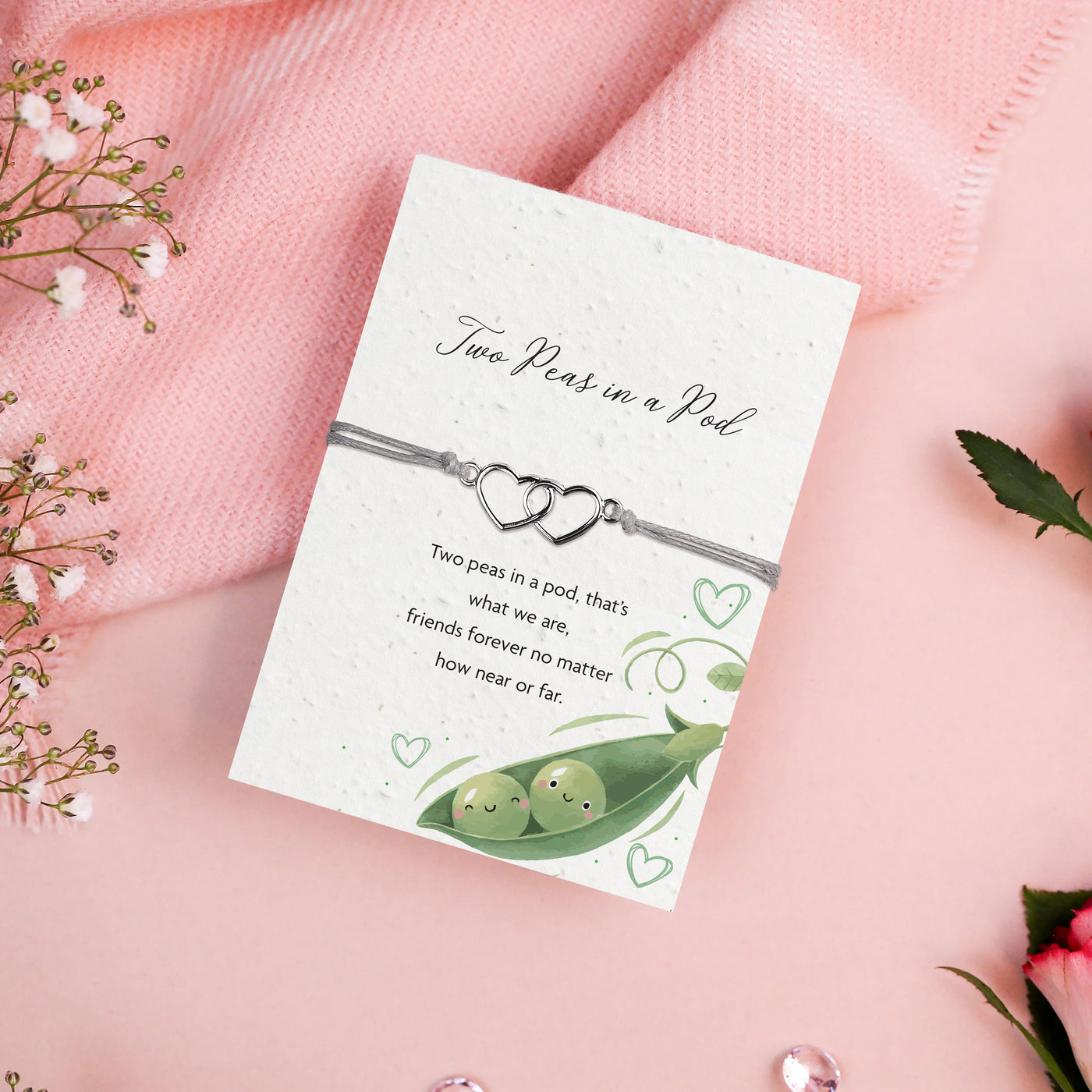 Seeded card with a two peas in a pod illustration and silver heart bracelet with grey cord, reading 