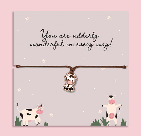 Adjustable cord bracelet with cute cow charm displayed on Udderly Wonderful message card, fun friendship jewellery gift with positive quote on pastel background.