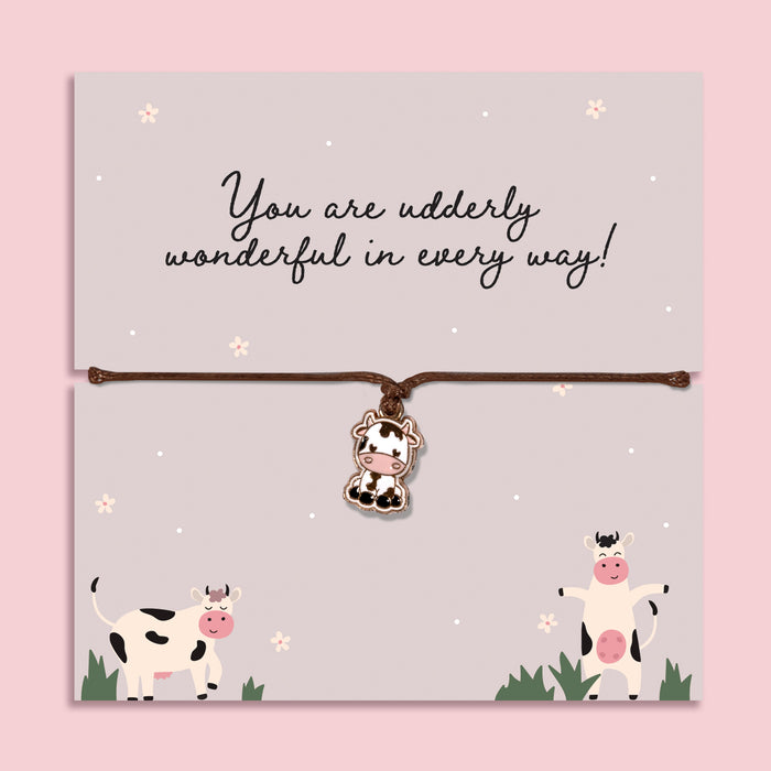 Adjustable cord bracelet with cute cow charm displayed on Udderly Wonderful message card, fun friendship jewellery gift with positive quote on pastel background.