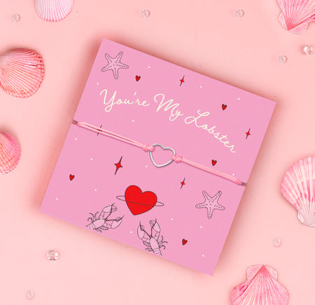 
A pink adjustable bracelet featuring a dainty silver-plated heart charm, displayed on a pink backing card with the message 