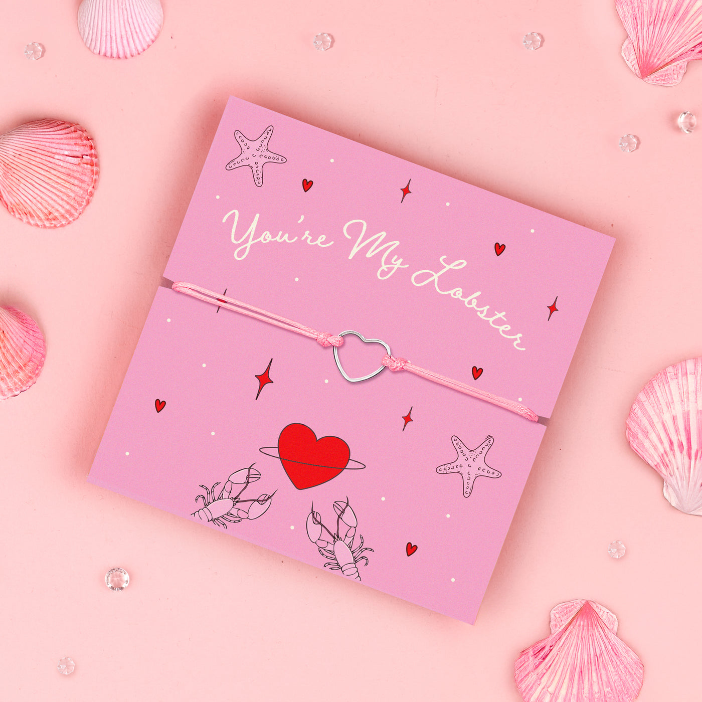 
A pink adjustable bracelet featuring a dainty silver-plated heart charm, displayed on a pink backing card with the message 