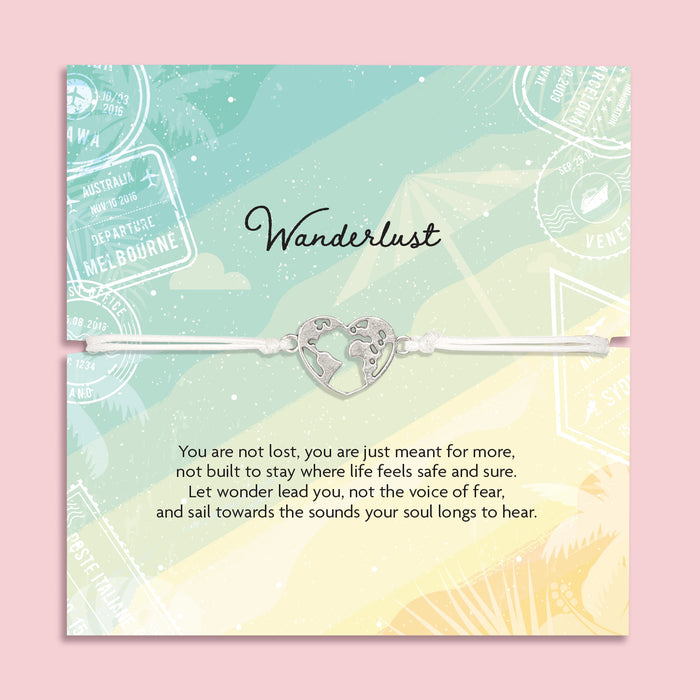 Adjustable white cord Wanderlust bracelet with a silver world map heart charm displayed on a travel-themed poem card and presented in a luxury white butterfly envelope.