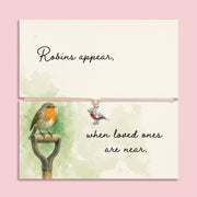 Memorial bracelet with silver robin charm and pink cord, displayed on a sentimental card reading “Robins appear, when loved ones are near,” with soft green watercolour and robin illustration.