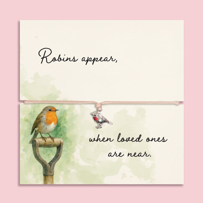 Memorial bracelet with silver robin charm and pink cord, displayed on a sentimental card reading “Robins appear, when loved ones are near,” with soft green watercolour and robin illustration.