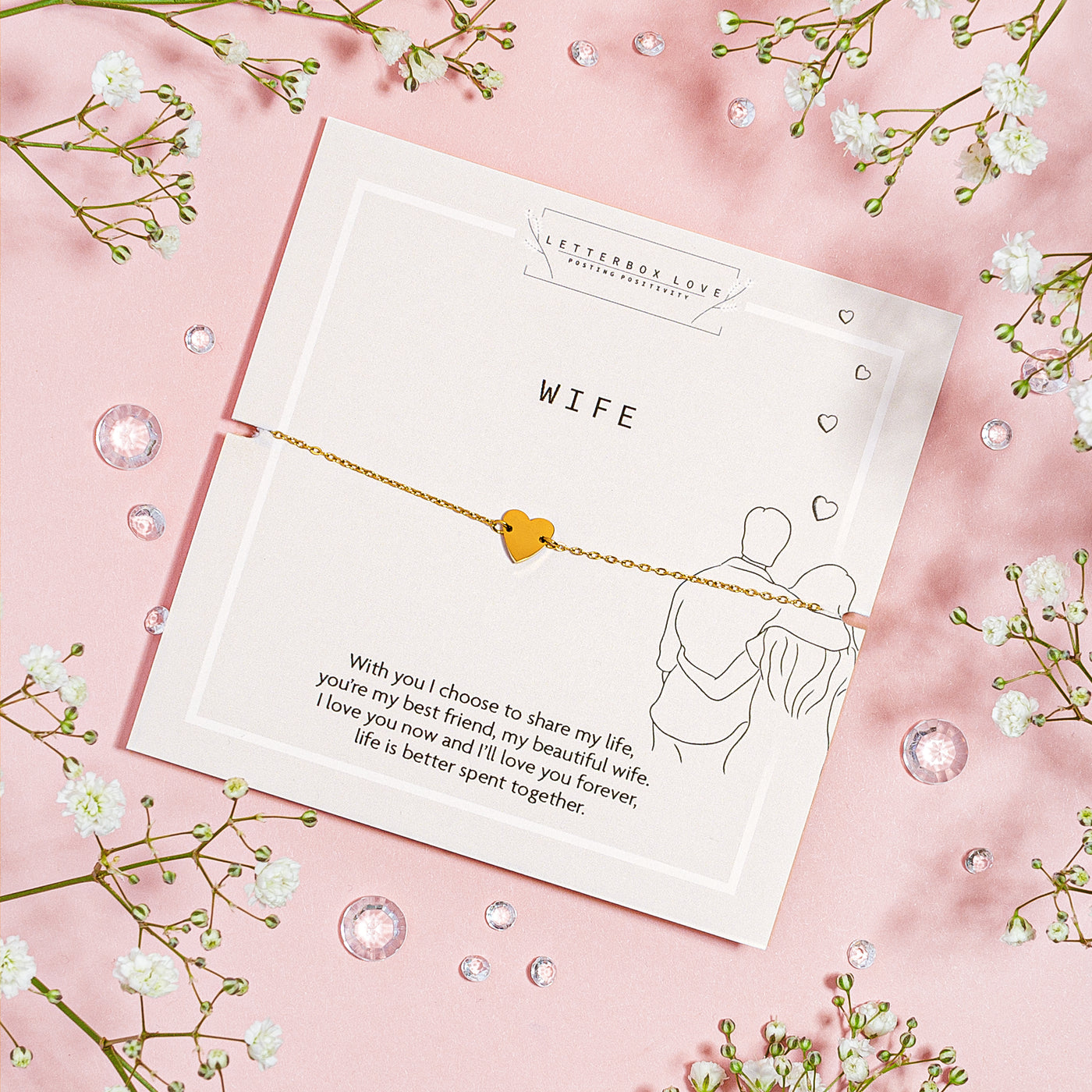 A dainty gold bracelet with a small, solid heart charm presented on a white card with the word 'WIFE' in bold, centered text. Below the bracelet, a loving message to a wife is printed, expressing lifelong commitment and affection.