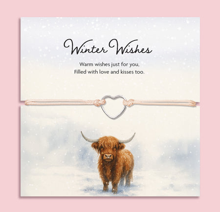 Beige cord bracelet with a silver-tone heart charm, displayed on a winter-themed card featuring a Highland cow in a snowy scene, with the words 'Winter Wishes – Warm wishes just for you, filled with love and kisses too'.