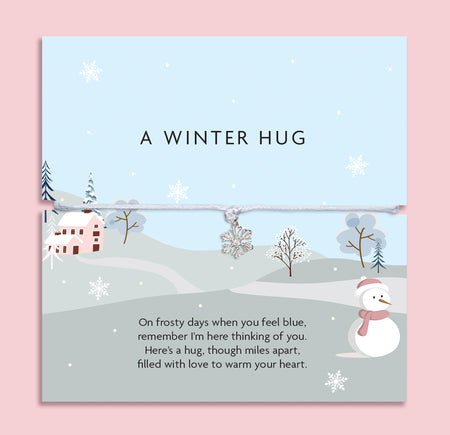 A winter-themed card with a snowman, snowflakes, and a soft grey string bracelet featuring a silver snowflake charm, a sentimental “A Winter Hug” gift designed to comfort and connect loved ones during the colder months.