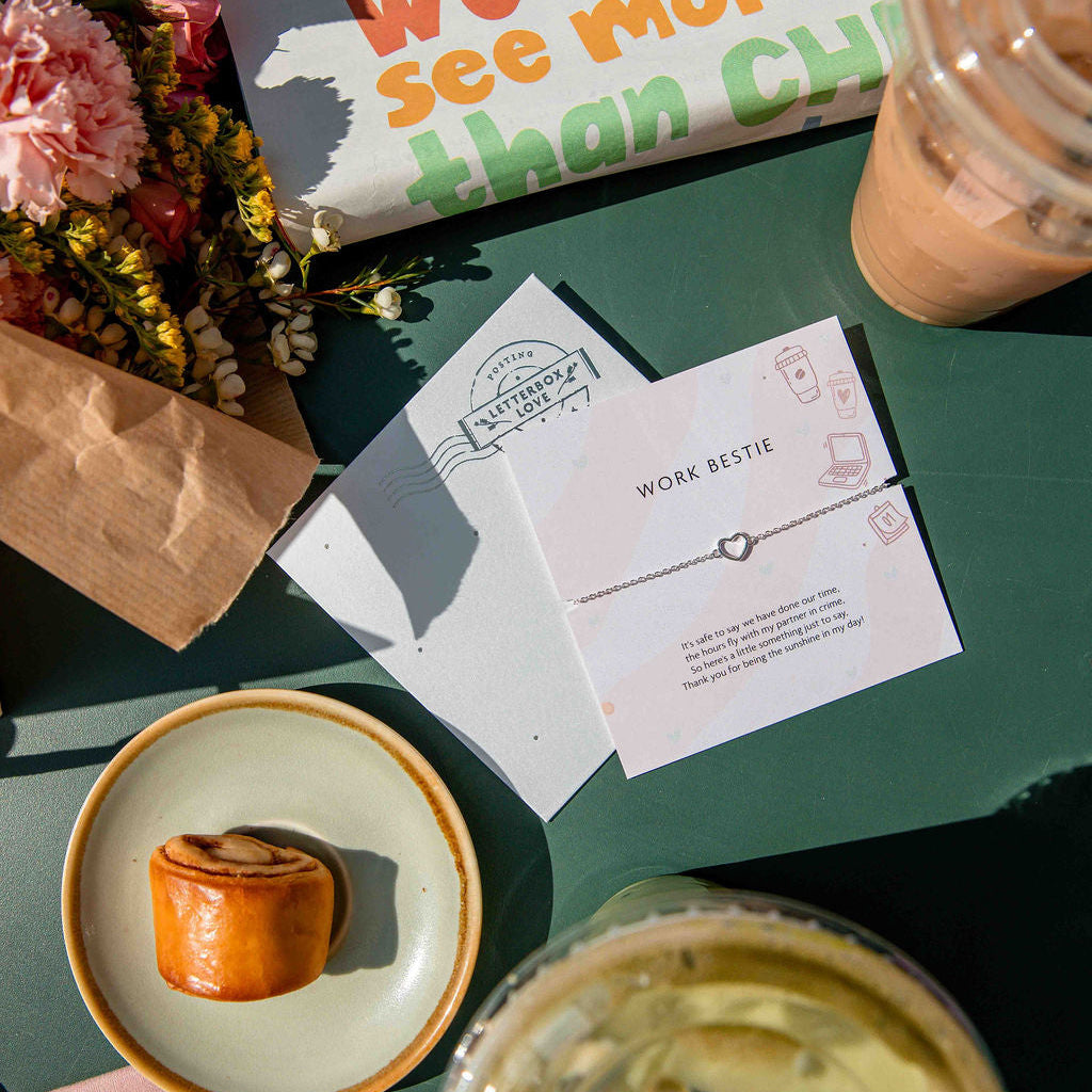 Table setting with a pastry, coffee, flowers, and a work bestie card on a green surface.