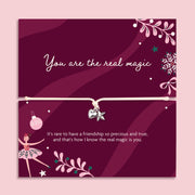 A square pink card with a thin cord bracelet across the center, decorated with white text, ballerina illustrations, stars, and floral motifs on a dark magenta background. A heartfelt gift for Xmas.