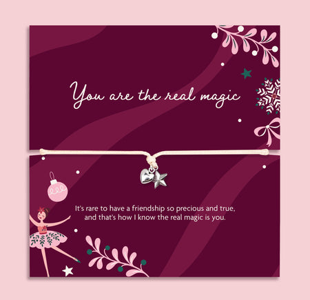 A square pink card with a thin cord bracelet across the center, decorated with white text, ballerina illustrations, stars, and floral motifs on a dark magenta background. A heartfelt gift for Xmas.