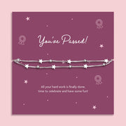 A silver star-themed beaded bracelet displayed on a purple 'You've Passed!' milestone card, set against a light pink background.
