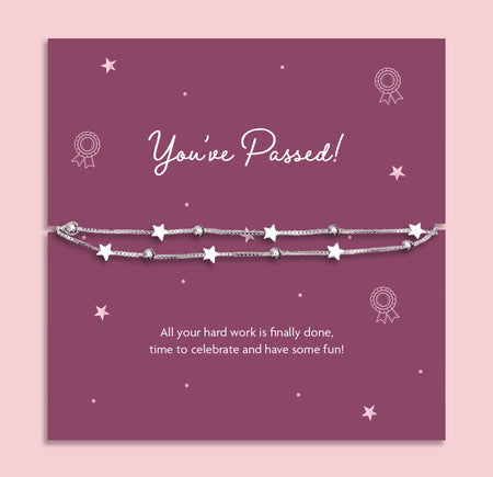A silver star-themed beaded bracelet displayed on a purple 'You've Passed!' milestone card, set against a light pink background.