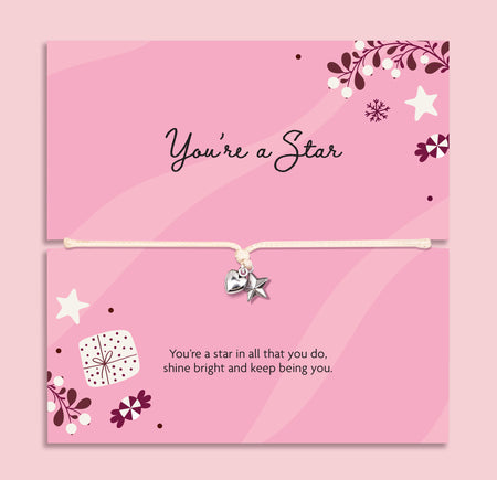 Pink card bracelet gift set with a silver heart and star charm on a cord, shown in two stacked cards with decorative stars, flowers, and inspirational text. The card reads 'you're a star', a heartfelt gift for her this Christmas