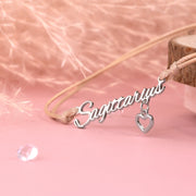 Friendship jewellery reading "Sagittarius" on a beige string. Bracelet with zodiac design on a pink background and a heart charm. Star sign jewellery for a friend