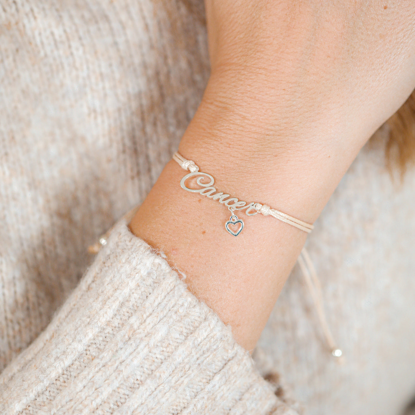 Silver bracelet with 'Cancer' star sign on a wrist against a neutral background. Zodiac jewellery for her.