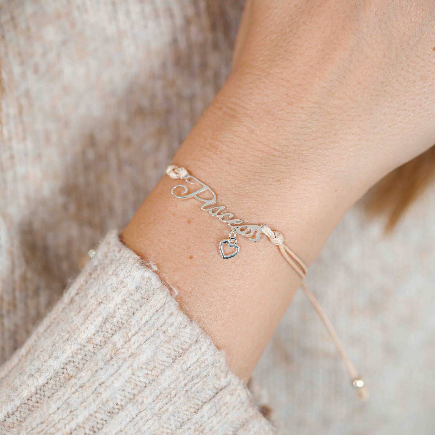 A woman wearing a delicate bracelet with the word “Pisces” and a small heart charm, a meaningful zodiac bracelet gift for her.