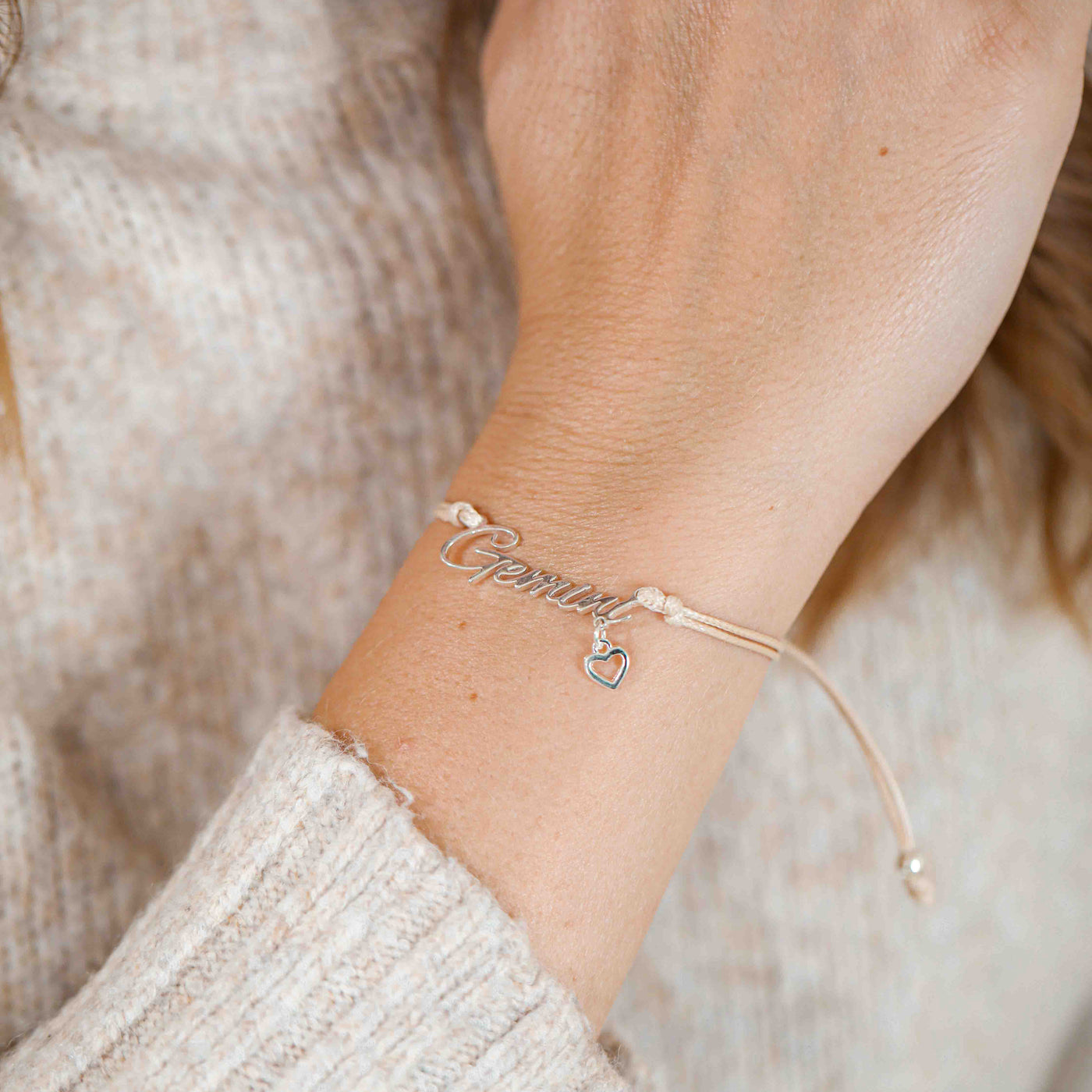A woman wearing a delicate bracelet with the word “Gemini” and a small heart charm, making a thoughtful zodiac-themed gift.