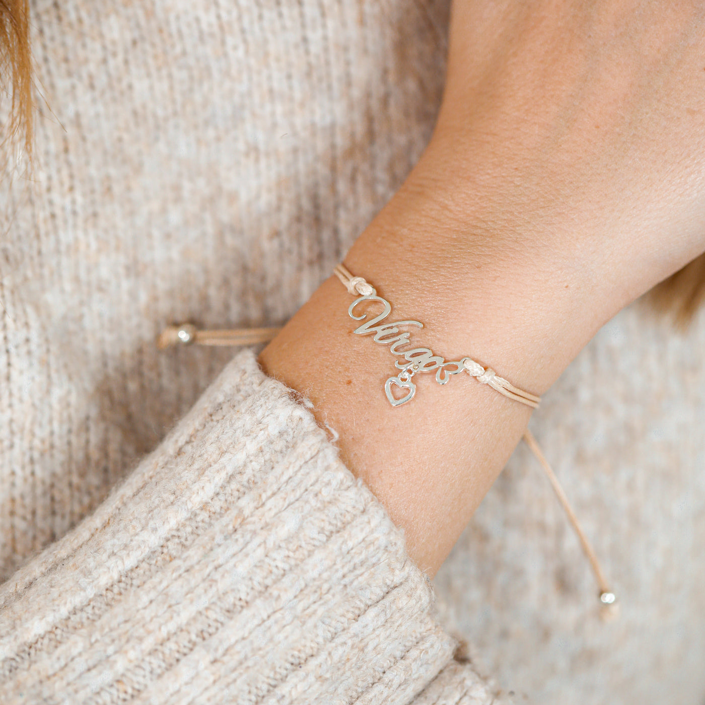 Gold bracelet with heart and Virgo charm on a woman's wrist against a neutral background. A starsign gift for her.
