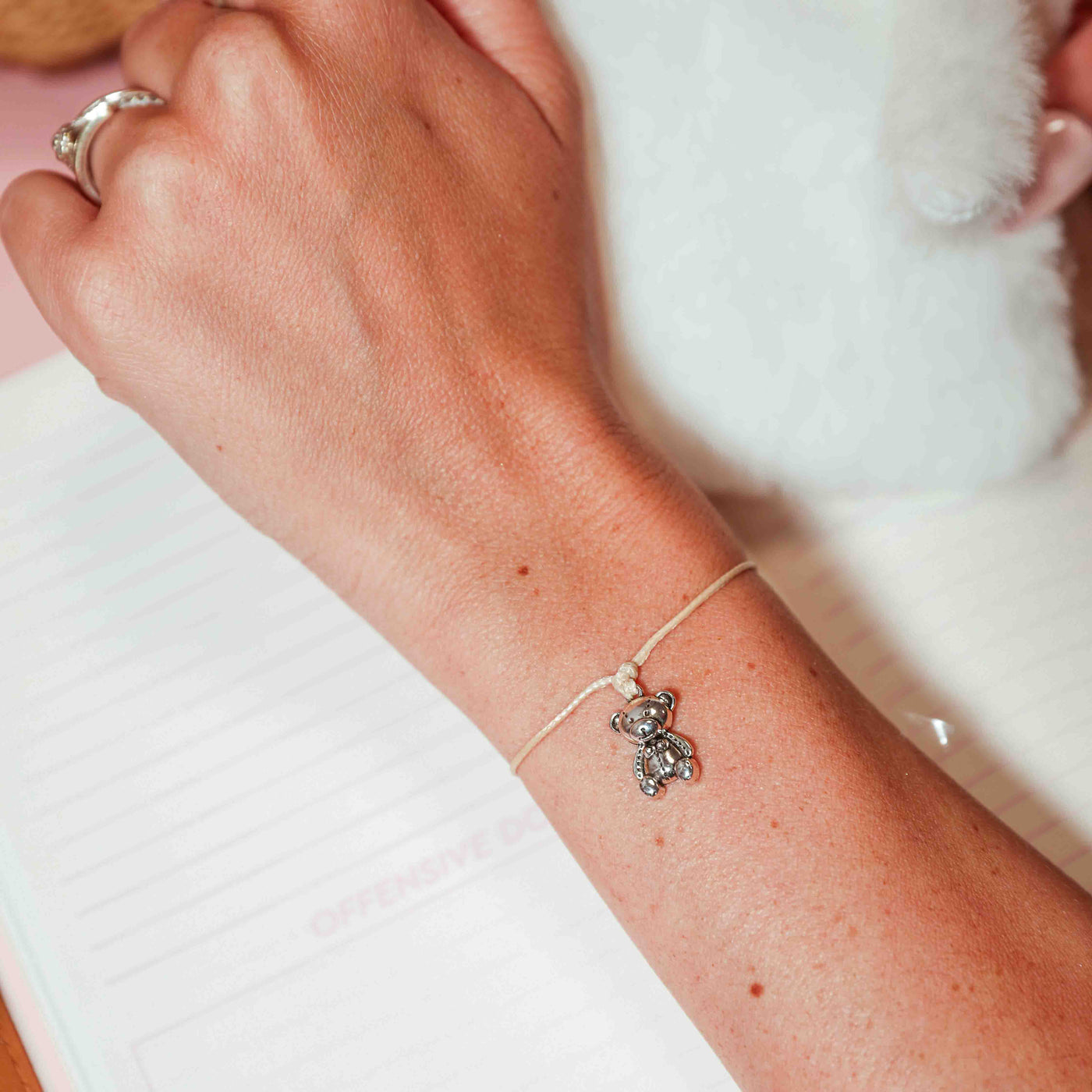 Close-up of a wrist wearing a delicate bracelet with a small bear charm on a light background