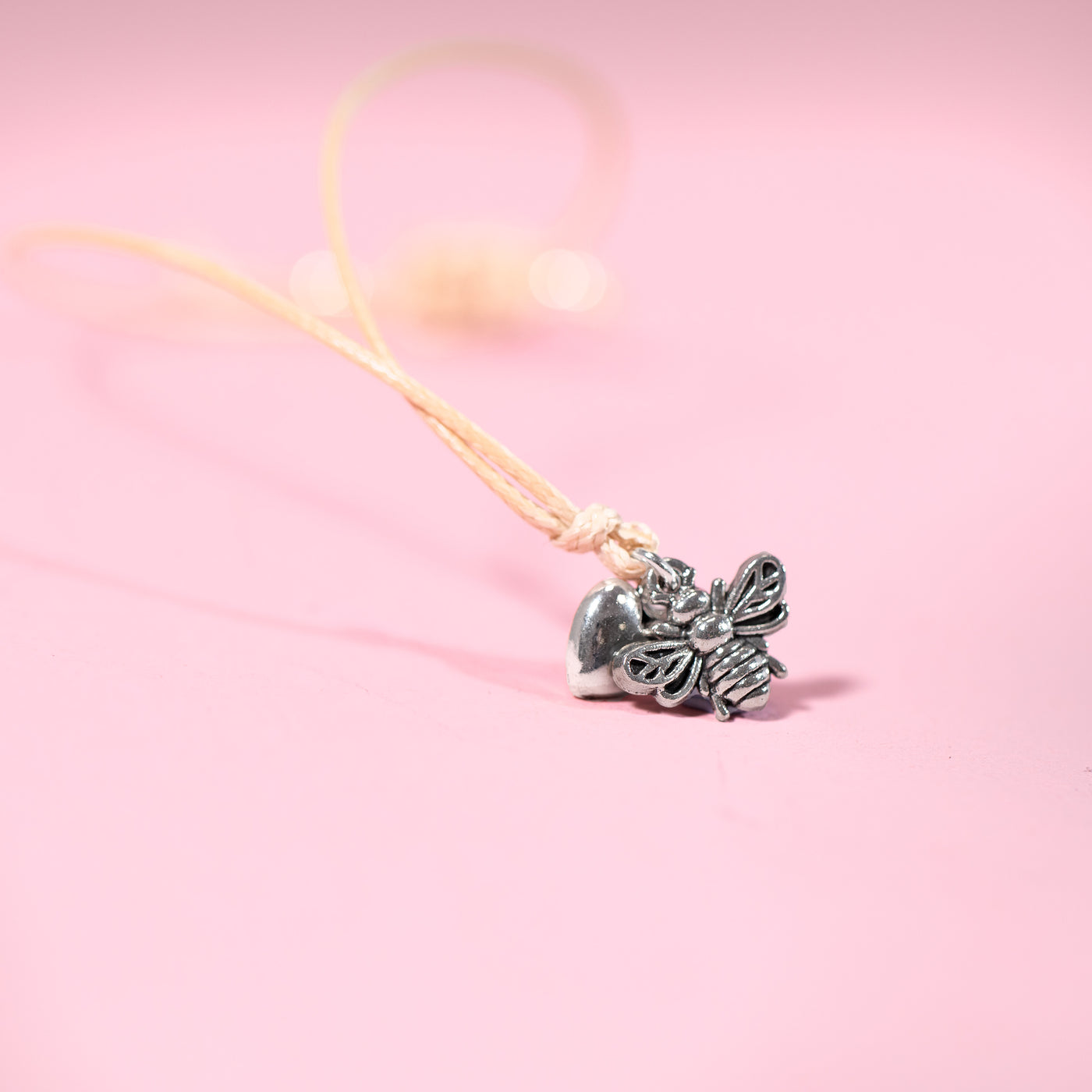 Silver bee-shaped pendant on a pink background