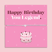 Happy Birthday You Legend bracelet with heart charm on adjustable cord displayed on pink birthday card with cake illustration, fun birthday gift