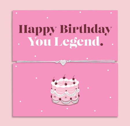 Happy Birthday You Legend bracelet with heart charm on adjustable cord displayed on pink birthday card with cake illustration, fun birthday gift