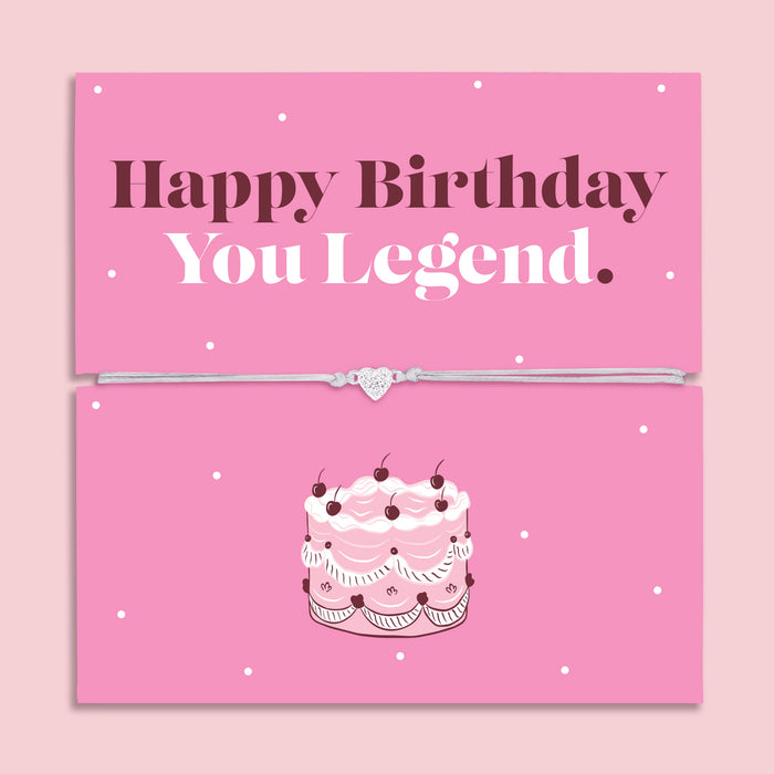 Happy Birthday You Legend bracelet with heart charm on adjustable cord displayed on pink birthday card with cake illustration, fun birthday gift