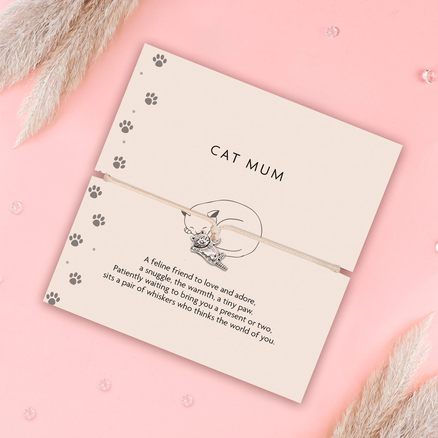Cat-themed bracelet on a decorative card with paw prints and text on a pink background